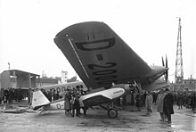 A50ce D-1842 shelters under the wing of big sister G38 D-2000 in May 1930 Bundesarchiv Bild 102-09778, Berlin-Tempelhof, Flugzeuge Junkers G 38 und A 50.jpg