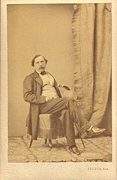 Photographie de Félix Milliet, posant assis sur une chaise, les jambes croisées.