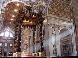  Photo shows the baldachin standing in the centre of the church, viewed looking towards the nave. There is an altar beneath it which is has a red and gold frontal cloth decorated with large crosses.