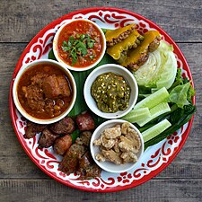 Un échantillon de la cuisine du nord de la Thaïlande (Lanna). En commençant par le haut : nam phrik ong, à gauche le kaeng hangle, au milieu le nam phrik num (purée de piments verts grillés, échalotes et ail), en dessous un petit bol de kaep mu (couennes de porc frites), avec à gauche des tranches de sai ua (saucisse de porc épicée grillée) et de si khrong mu thot (morceaux de côtes de porc frites).