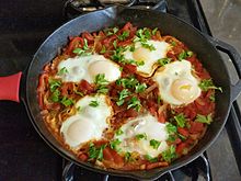 Shakshouka dengan lima telur goreng di atas saus tomat pada sebuah penggorengan besi