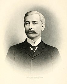 A black-and-white lithographic portrait of a middle-aged, mustached man from the shoulders up, wearing a suit, with a necktie