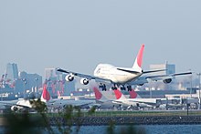 Pesawat sedang mendarat dengan pemandangan terminal bandara di latar belakang