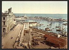 Photo coloriée d'un quai et d'une rade avec navires, entourés de bâtiments blancs