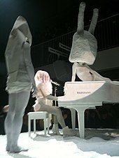 A picture of Lady Gaga on a piano surrounded by statues