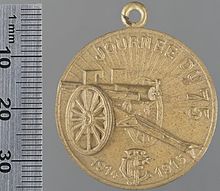 Photo d'une médaille dorée représentant un canon, le soleil se levant en arrière-plan.