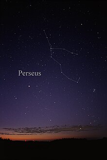 Barevná fotografie noční oblohy: dole obzor zapadajícího slunce s končícími červánky a nad nimi se táhnoucí slabou vrstvou mraků na jinak bezoblačné obloze. Na tmavě modré obloze plné hvězd vyznačeno souhvězdí Persea prostřednictvím spojení jeho hvězd bílými čarami: od vrchní hvězdy vede čára dolů mírně doprava, na druhé hvězdě se větví a jedna větev pokračuje mírně klikatě stejným směrem přes dalších šest hvězd, přičemž na páté se ohýbá nahoru a tvoří jakýsi ocásek; druhá větev se stáčí doprava téměř do horizontální pozice postupně klesající dolů přes další tři hvězdy
