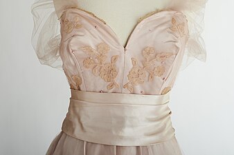 Une robe en satin rose avec une superposition de dentelle appliquée Carrickmacross avec un motif de papillon et de petites perles.