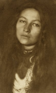 Тонированное сепией изображение бюста индейской женщины, смотрящей прямо в камеру.