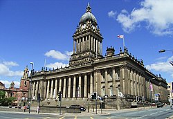 An impressive free-standing stone-built civic building on a sloping site with steps up to a colonnade. Above the parapet is a square clock-tower, also colonnaded, with an elongated lead-covered dome with concave sides and a cupola on top.