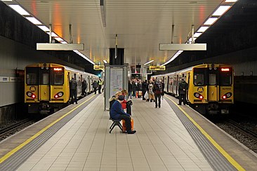 Two yellow trains on either side of a platform in an underground station