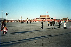 Groups of people wander around Tiananmen Square in the late afternoon. The eponymous Tiananmen, literally "Gate of Heavenly Peace", sits in the background.