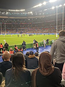 Femme voilée de dos dans les premiers rangs des spectateurs lors d'une rencontre de rugby au Stade de France.