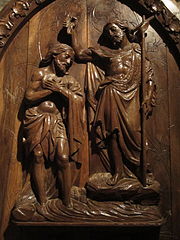 Photo en couleur d'un panneau de bois sculpté représentant deux personnages, l'un, en toge, versant de l'eau sur la tête de l'autre, en pagne