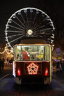 Vánoční šalina na zastávce Česká před kostelem sv. Tomáše na Moravském náměstí. V pozadí svítící vánoční kolo.