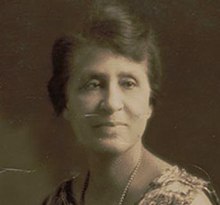 Photograph of a black woman in a sleeveless sheath wearing pearls.