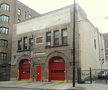 Un bâtiment en béton gris avec des grandes portes rouges et un drapeau des États-Unis en façade.