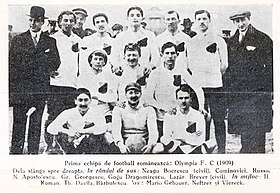 kelompok dari 11 laki-laki dalam tiga baris, duduk, berlutut dan berdiri, berpakaian hitam dan putih football kit, diapit oleh 2 pria dalam setelan