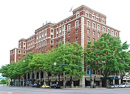 A nine-story hotel made of red brick surrounded by green trees growing in the sidewalk around its perimeter