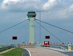 A cable-stayed tower with barriers and flashing lights on the road deck beneath