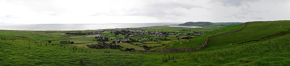 Панорама валлийского городка Тивин, на котором видно, что он расположен между холмами, а за ним море. На заднем плане виден резервуар.