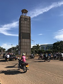 Une tour en pierre donnant sur une rue où avancent de nombreux motocyclistes.