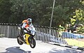 Hervé Gantner wearing a orange high-visibility vest riding a motorcycle on Ballaugh Bridge
