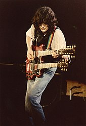 A colour photograph of Jimmy Page performing on stage with a double-necked guitar