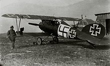 Photo en noir et blanc d'un homme adossé à l'aile d'un avion biplan.