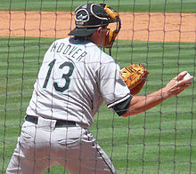 A man in a gray baseball uniform reading "Hoover" and "13" on the back and a black catcher's mask on his face throwing a baseball with his right hand