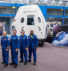 The Crew Dragon mockup (background) and four of the astronauts of its first two crewed missions (foreground), from left to right: Douglas Hurley, Robert Behnken, Michael S. Hopkins, and Victor J. Glover SpaceX Dragon 2 and astronauts 2018.jpg