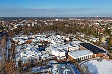 Luftaufnahme der Schulgebäude im verschneiten Winter, im Hintergrund ein bewaldeter Park und Wohnhäuser des Stadtteils Berlin-Zehlendorf