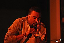 An image of a man singing into a microphone against red light.