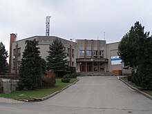 Betonová dvoupodlažní budova obecního úřadu v Mořkově stojící na mírném kopečku, k níž vede vyasfaltovaná komunikace lemovaná jehličnatými stromy.