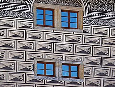 Vue des sgraffites en forme de bossages d'une façade, percée de quatre petites fenêtre à carreaux.