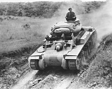 A tank cruises down an embankment in an open field while its commander stands out of the turret