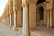 Portique oriental de la cour. Les colonnes de la façade, adossées à des piliers, sont coiffées de chapiteaux variés.