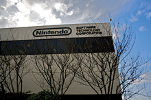 Серое невзрачное здание с надписью «Nintendo» на верхнем этаже и деревьями на переднем плане.