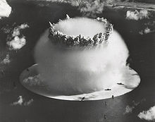 Аерофотозйомка ядерного вибуху, що підіймається з лагуни. Напівсферична хмара конденсації на поверхні має 1 mile (1,6 km) в діаметрі. Для порівняння, Кораблі флоту на передньому плані виглядають як іграшки для ванної.