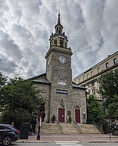 Fotografía en color de una iglesia urbana de granito flanqueada por pequeños jardines