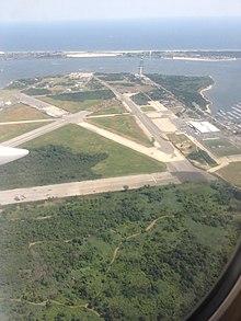 Вид с воздуха на взлетно-посадочные полосы среди травянистого поля с заливом на заднем плане