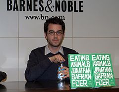 Fotografia barwna, mężczyzna siedzi przy stole, a przed nim stoi ksiażka w zielonej okładce z białymi literami na tejże