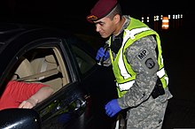 An American military policeman checks a driver's license at Fort Liberty, North Carolina U.S. Army Spc. David A. Morales, a military police officer with the 42nd Military Police Detachment, 16th Military Police Brigade, checks a driver's license at a safety checkpoint at Fort Bragg, N.C 131224-A-UK859-347.jpg