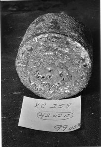 A rough-surfaced cylinder of metal with a paper in front of it, like a label