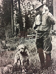 A man in a forest ranger uniform poses with his dog