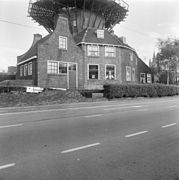 Photographie en noir et blanc d'une maison et d'une remise couronnés d'une galerie et longées par une route.