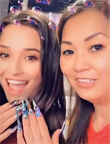 Two women, one holding up her hands to show crystal-studded nails