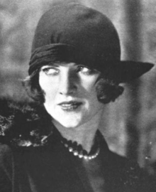 A young white woman with dark bobbed hair, wearing a dark cloche hat low over her brow