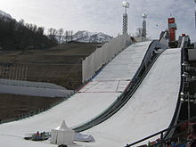 Une photographie en couleurs représentant des tremplins de saut à ski ornés des anneaux olympiques