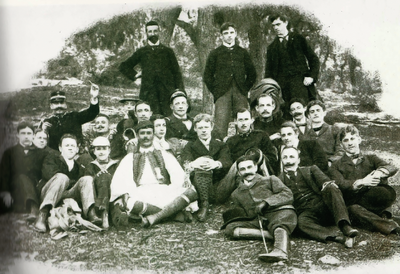 De nombreuses personnes sont assises ou allongées sur l'herbe et posent pour une photo de groupe.